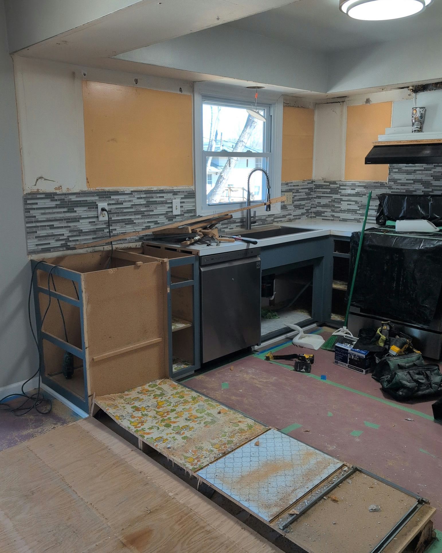 Kitchen under renovation. Unfinished cabinets, backsplash, sink, and window with exposed walls and flooring.