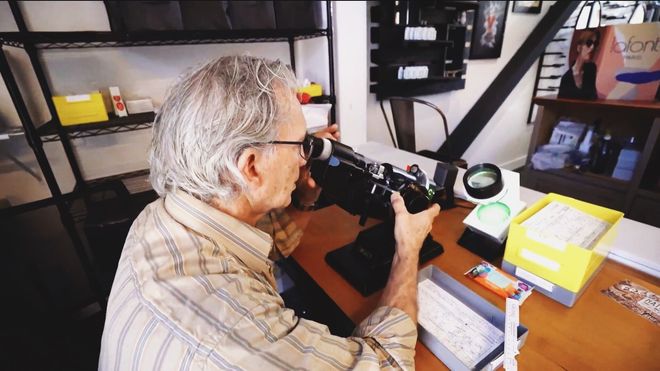 Gregor Owen, owner, sitting at a desk taking examining eye glass lenses