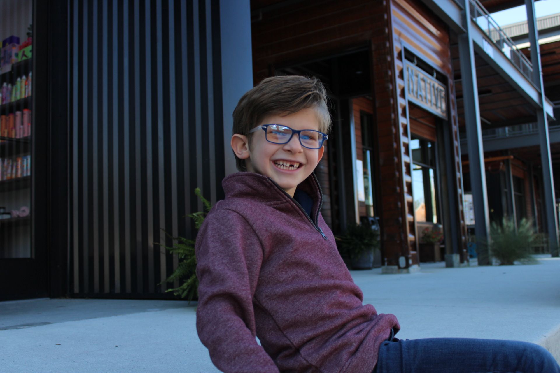 young boy smiling at the camera wearing glasses, exterior CustomEyes boutique eyewear and optician your child's vision needs