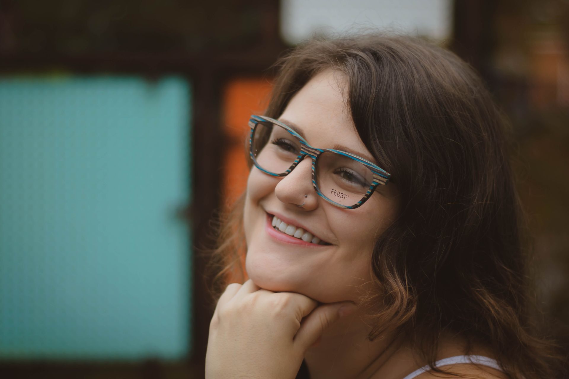 A woman wearing glasses is smiling with her hand on her chin.