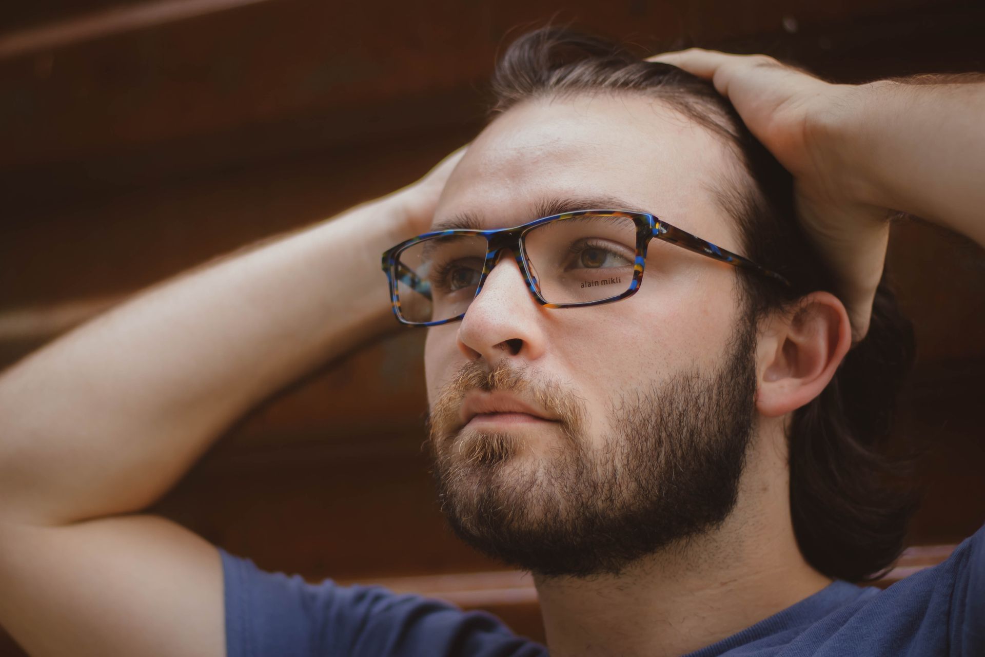 A man with a beard and Alian Mikli glasses is holding his hair back.