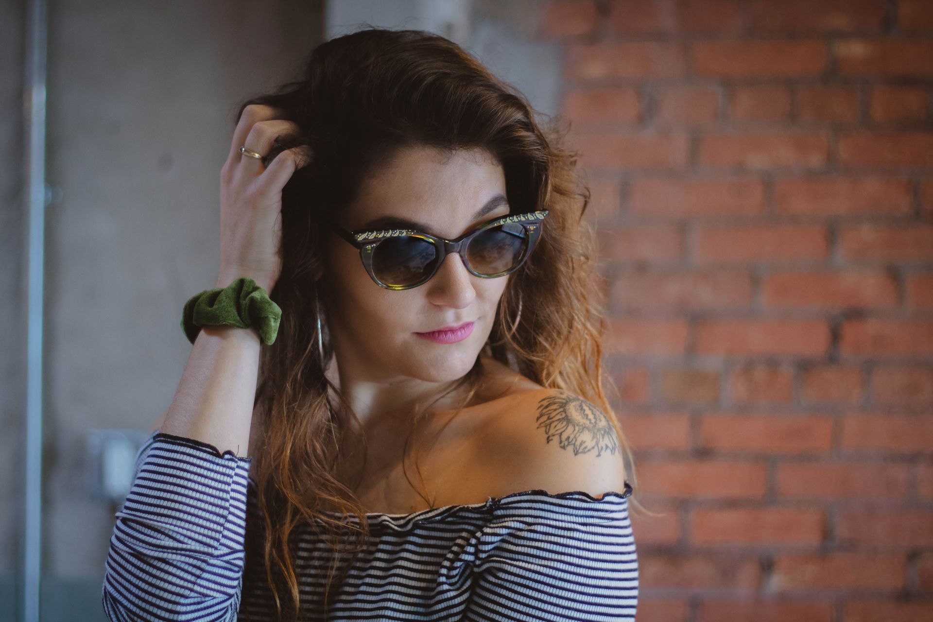 A woman wearing Francis Klein sunglasses and a striped shirt is standing in front of a brick wall.