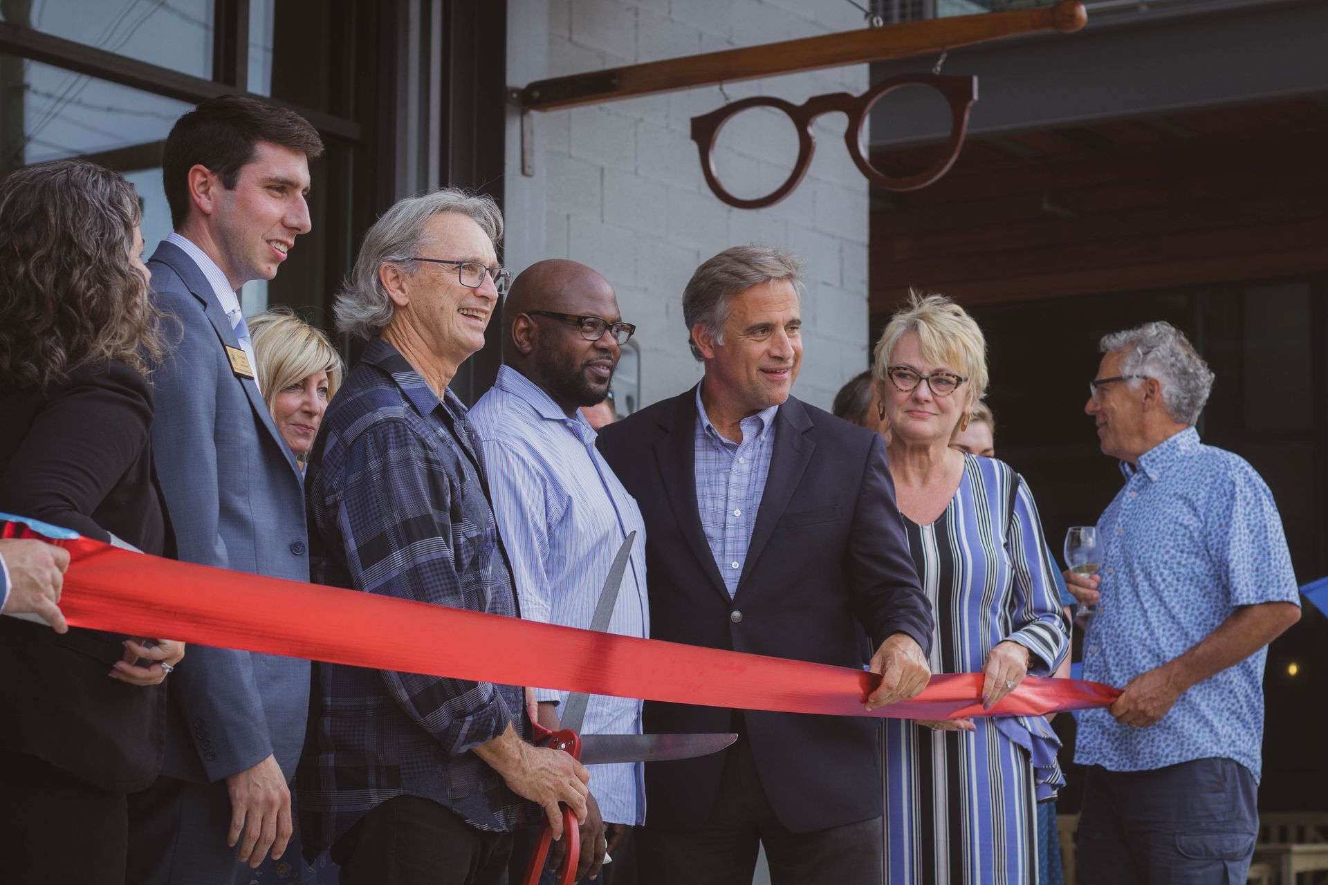 CustomEyes grand opening; owner Gregor Owen holding oversized scissors over a red ribbon. Mayor and others standing beside, smiling at camera