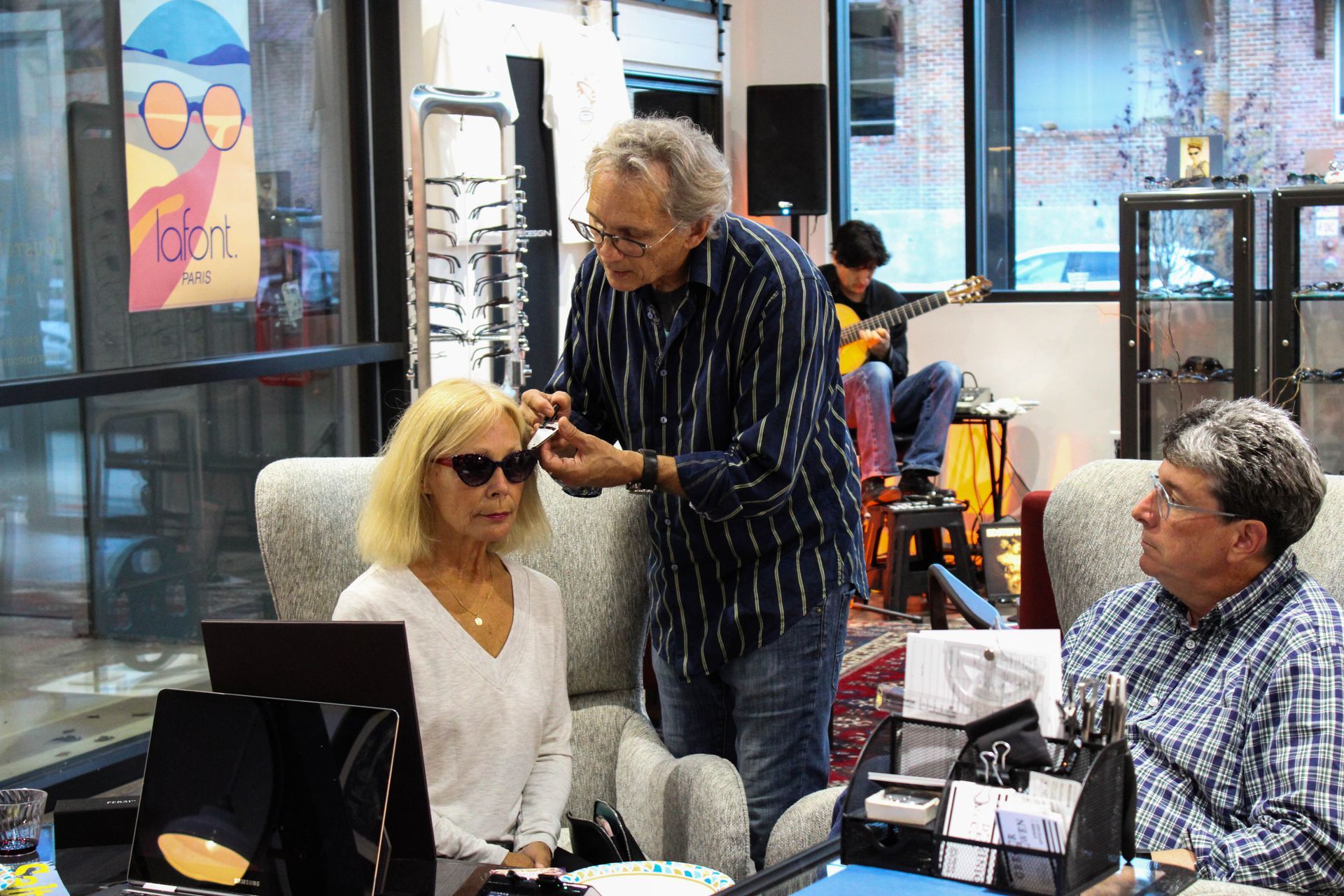 Optician Gregor Owen helping a woman with the fit of a pair of frames, interior CustomEyes shop