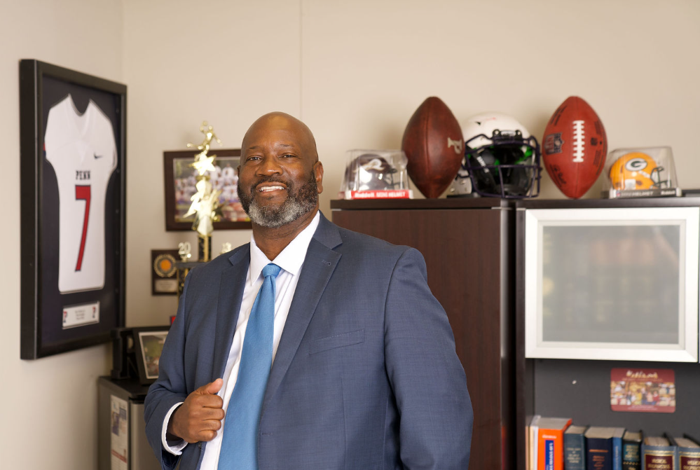A man in a suit and tie is standing in a room with footballs on the wall.