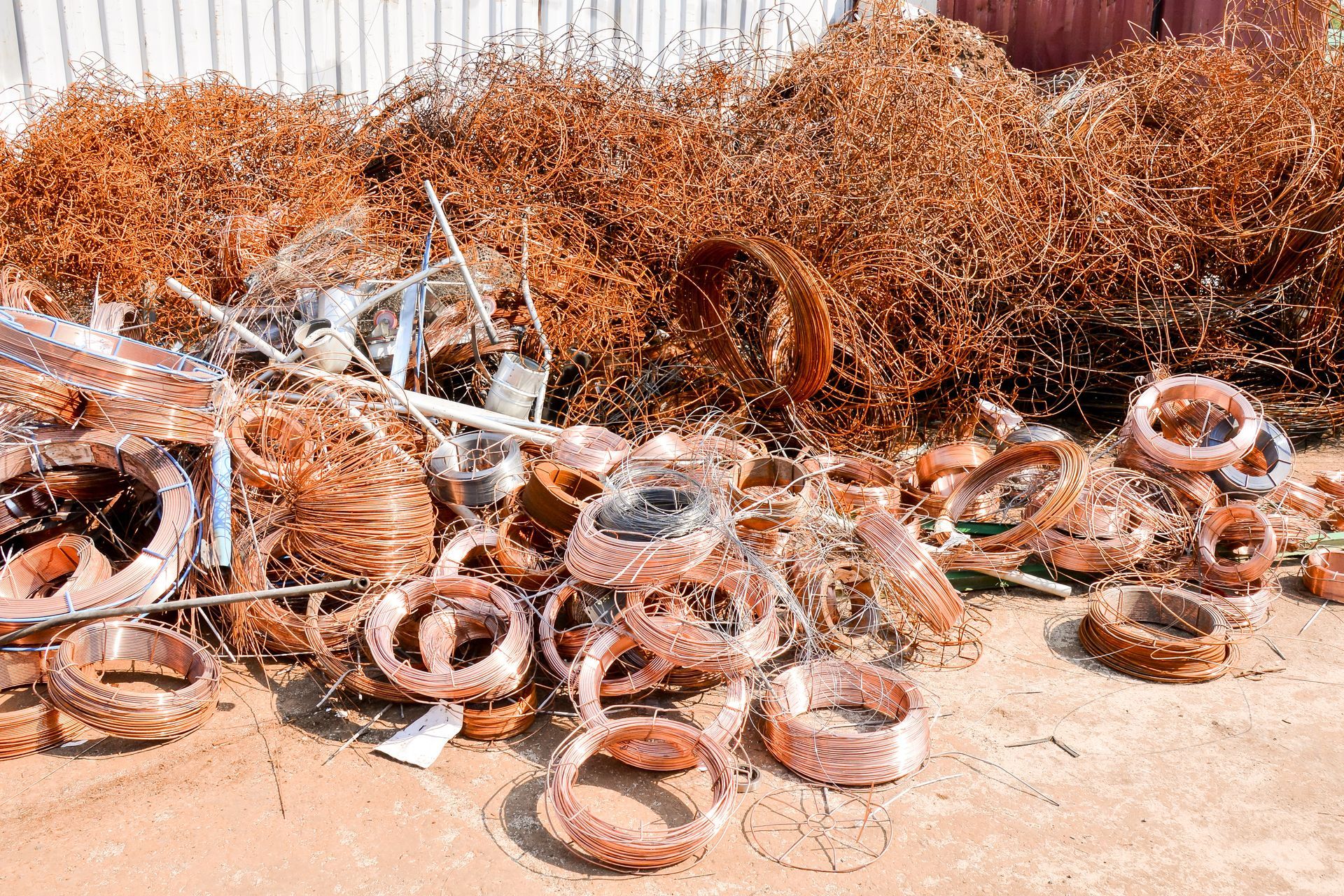 Pile of coiled copper wires and scrap metal collected for recycling at a yard.