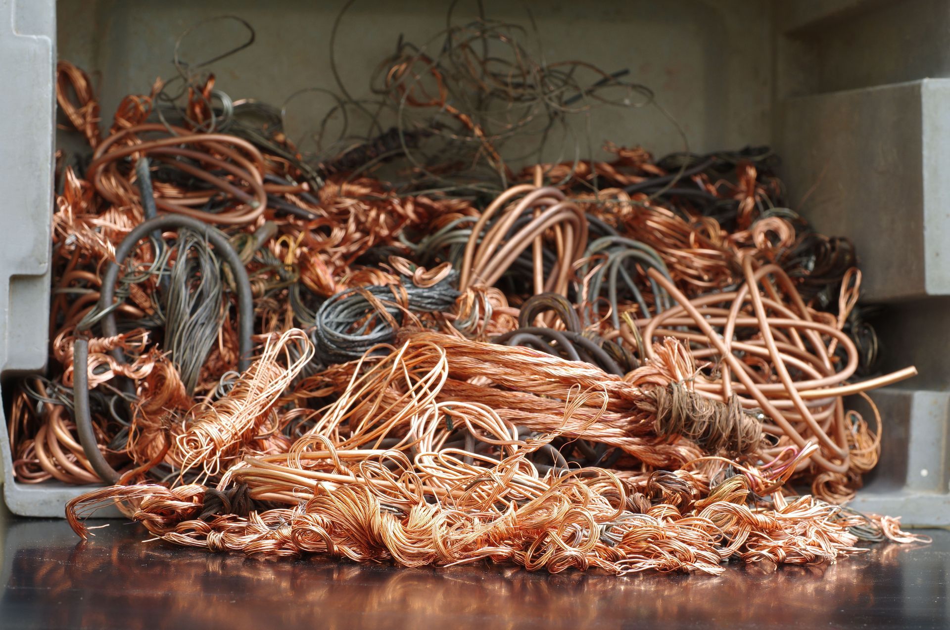 Copper wire scraps in a rectangular bin, varying shades of copper and grey.