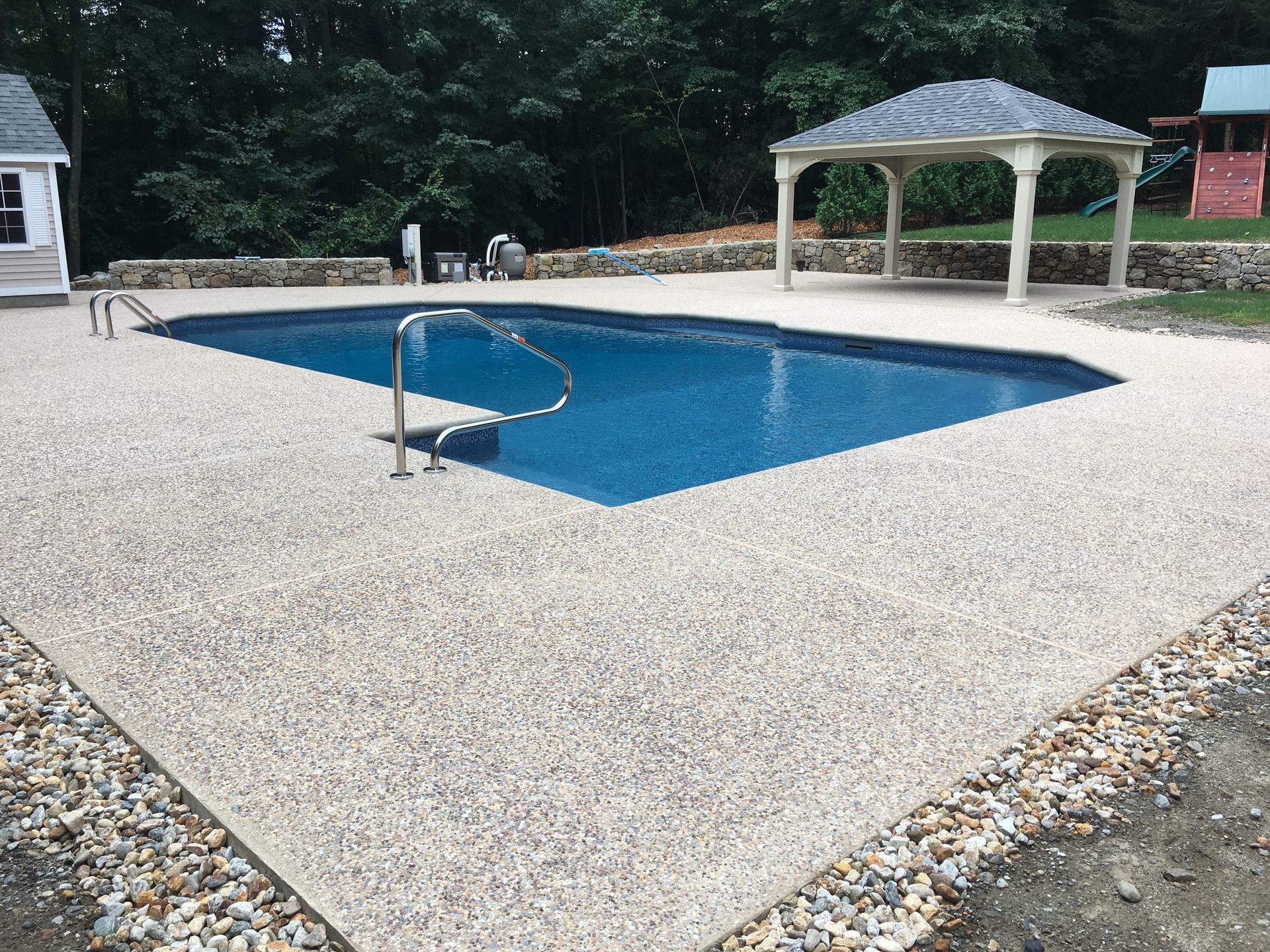 A large swimming pool is surrounded by a patio and chairs on a sunny day.