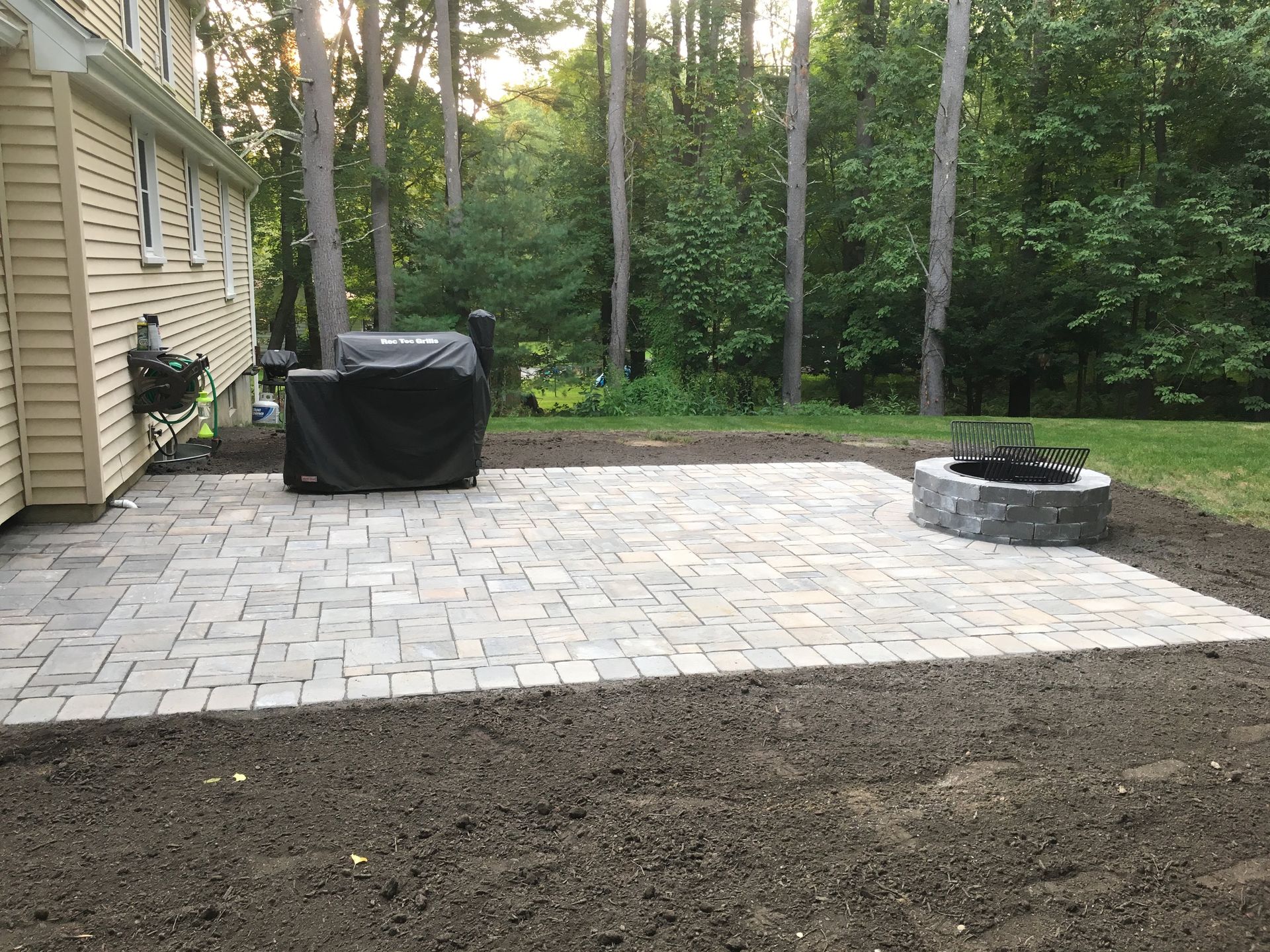 A patio with a grill and a fire pit in front of a house.