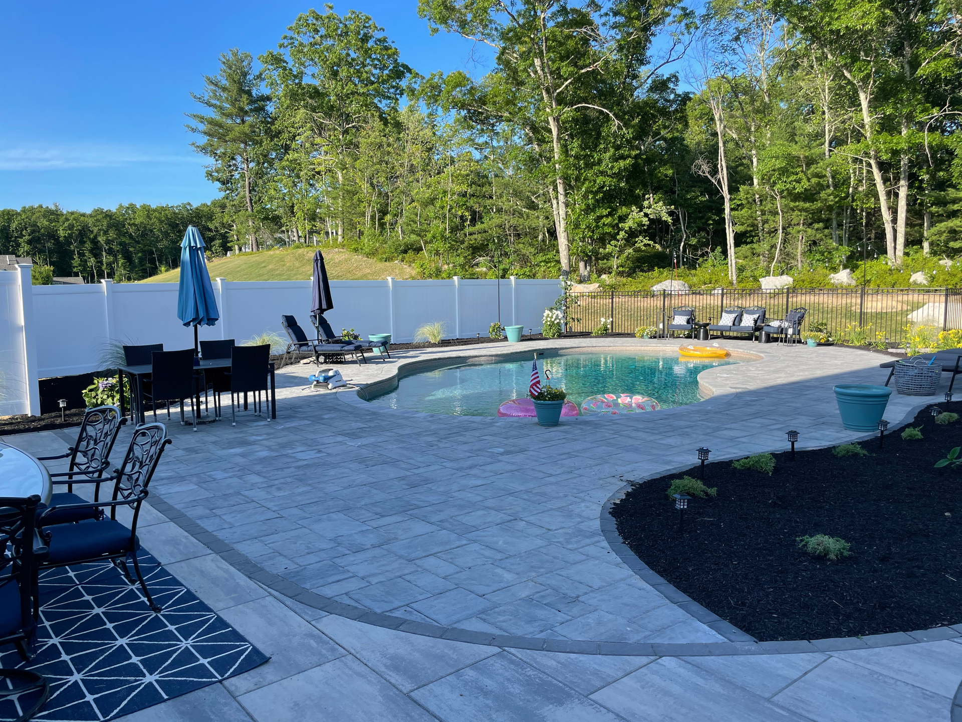 There is a large swimming pool in the backyard surrounded by trees.
