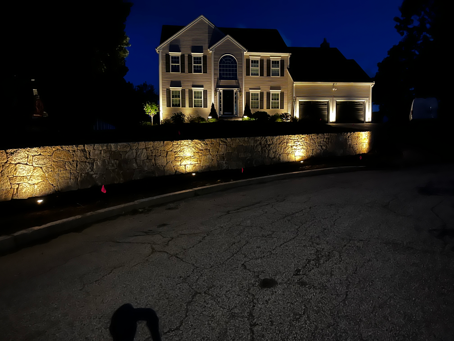 A large house is lit up at night with a stone wall