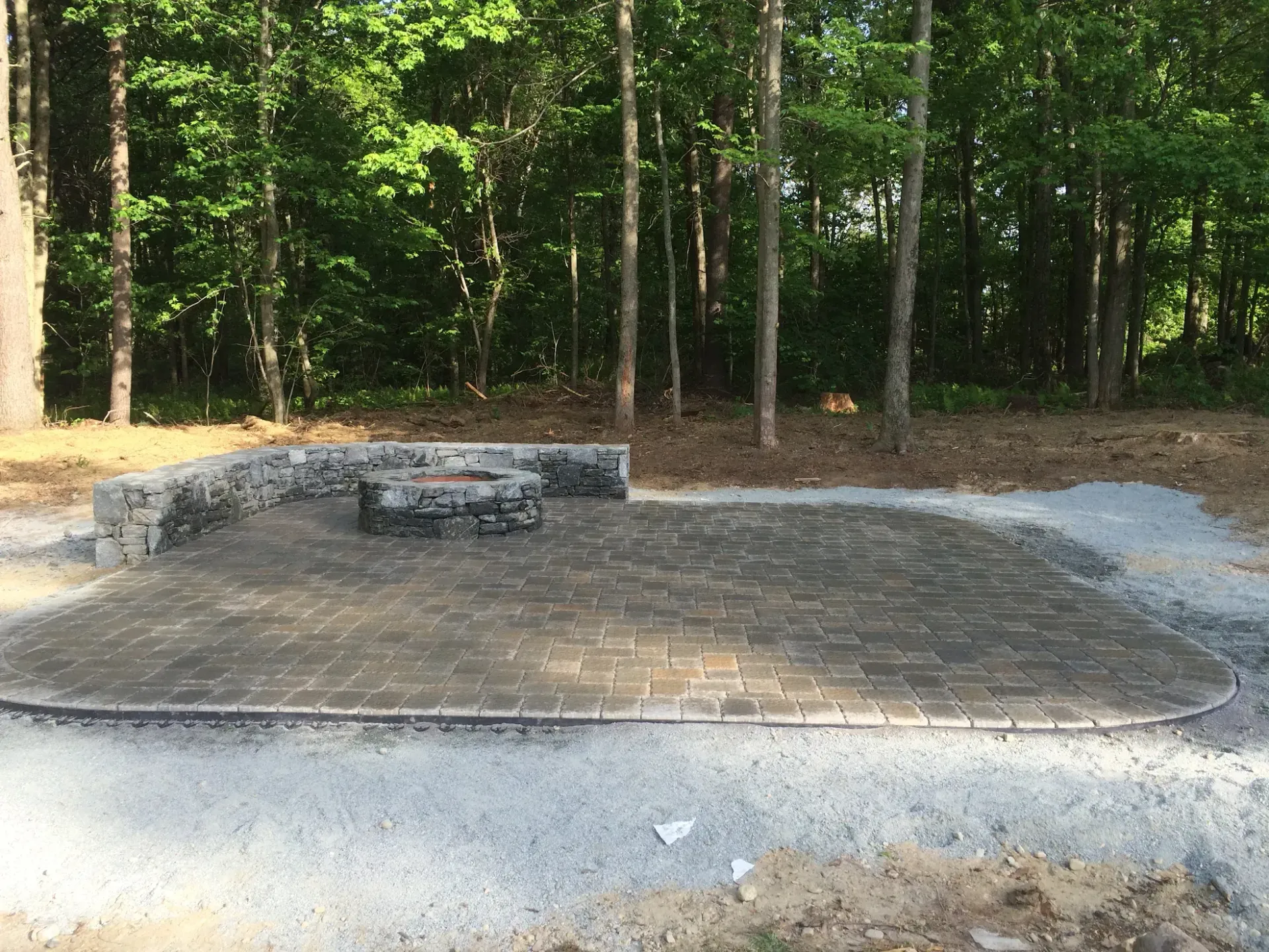 A patio with a fire pit in the middle of a forest.