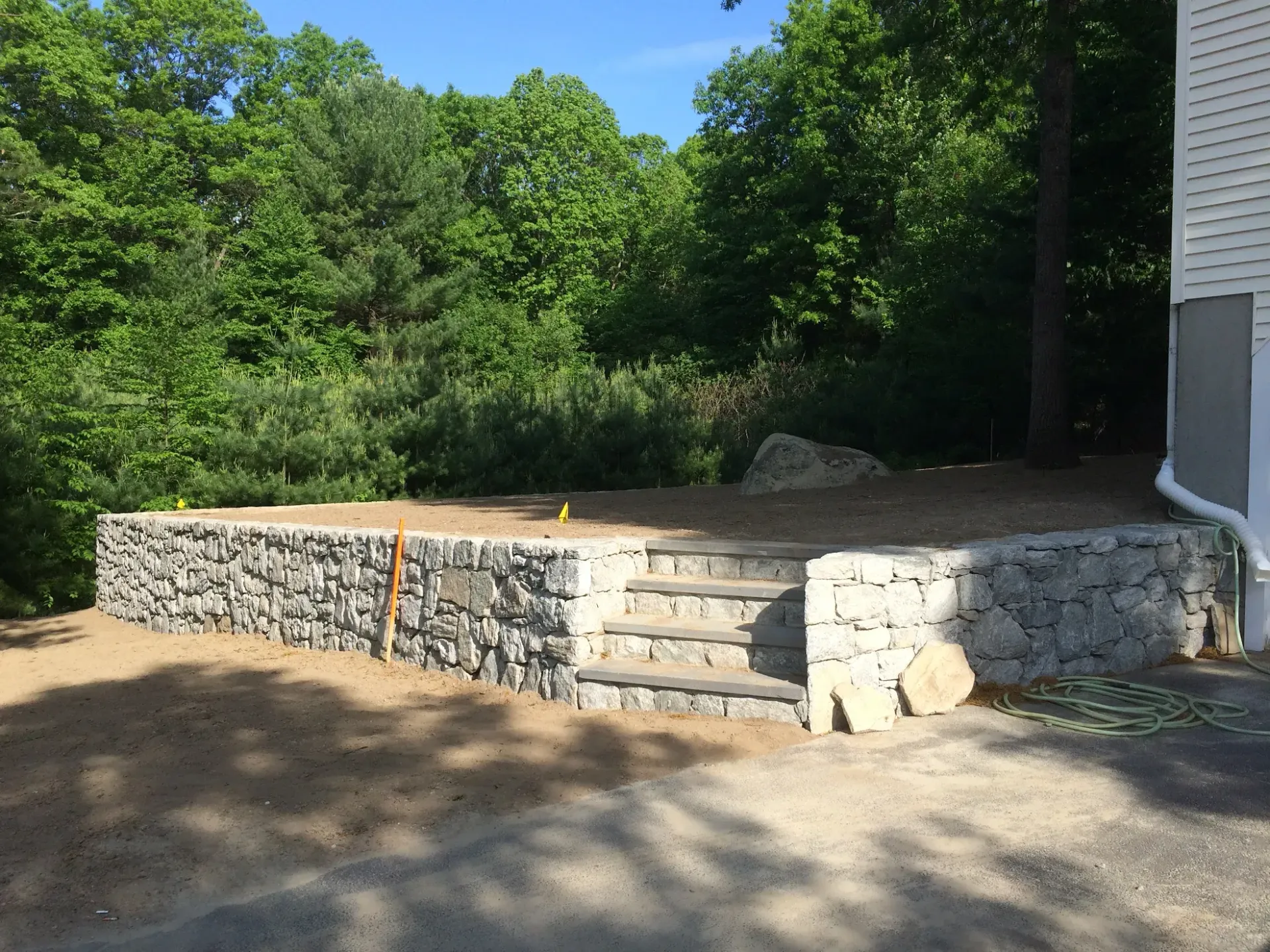 A stone wall with stairs leading up to it is in front of a house.