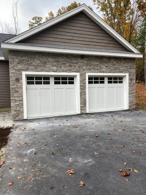 A garage with two white garage doors and a stone wall