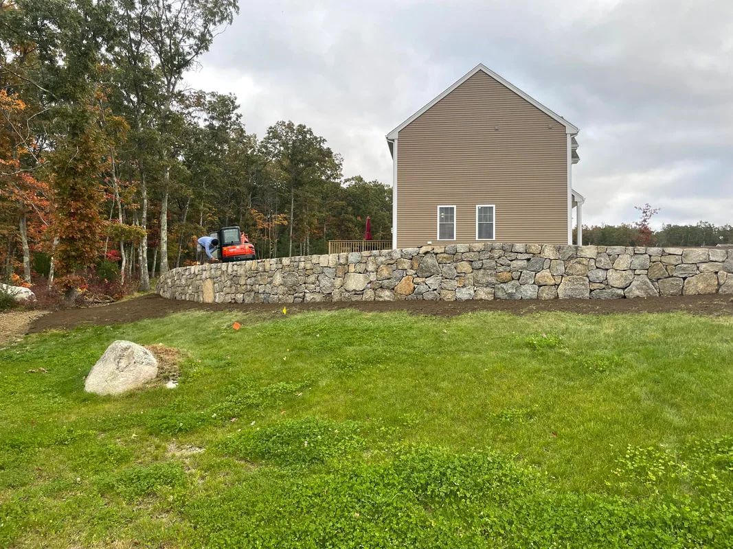 A house is sitting on top of a lush green field next to a stone wall.