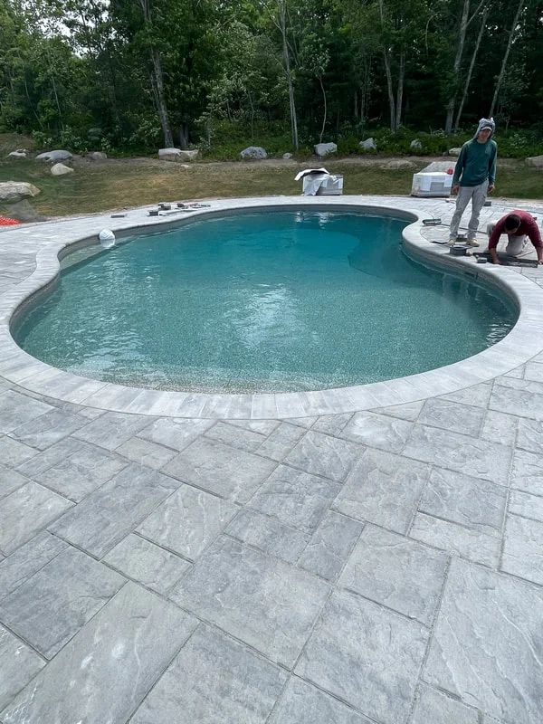 A man is standing next to a large swimming pool.