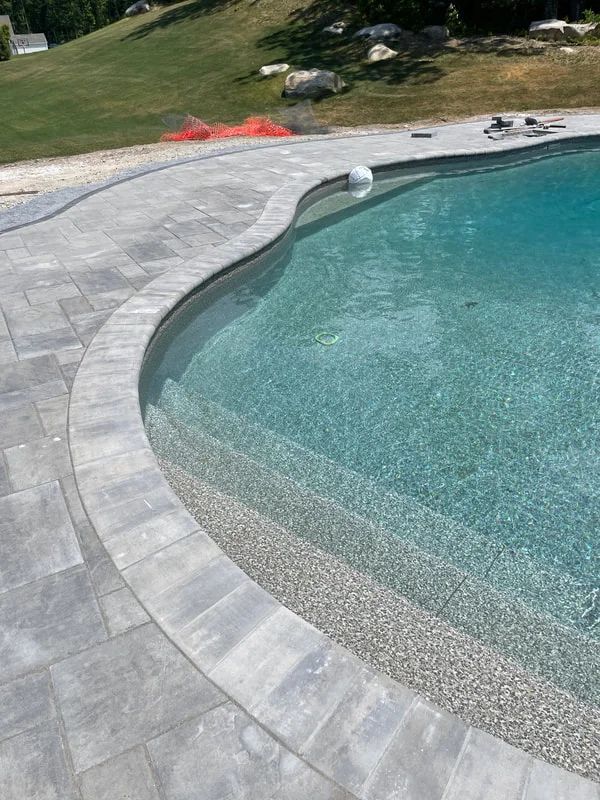 A swimming pool with steps and a patio next to it.