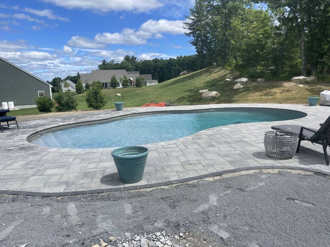 A large swimming pool is surrounded by a patio and chairs on a sunny day.