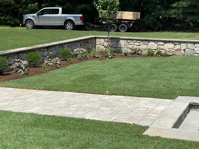 A truck is parked in the grass next to a stone wall.