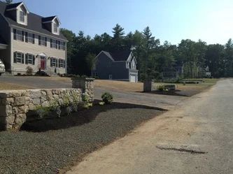 A large house is sitting on top of a dirt hill next to a road.