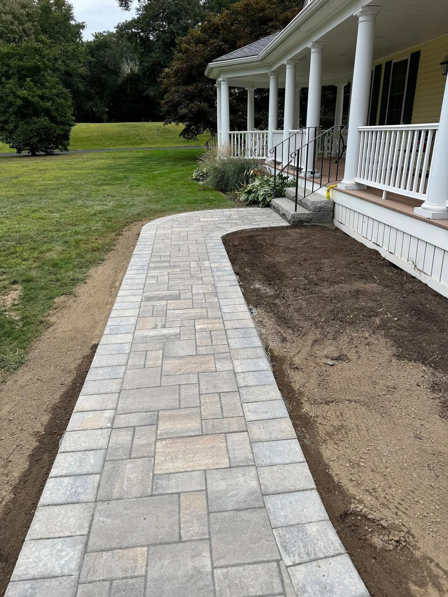 A brick walkway leading to a porch of a house.