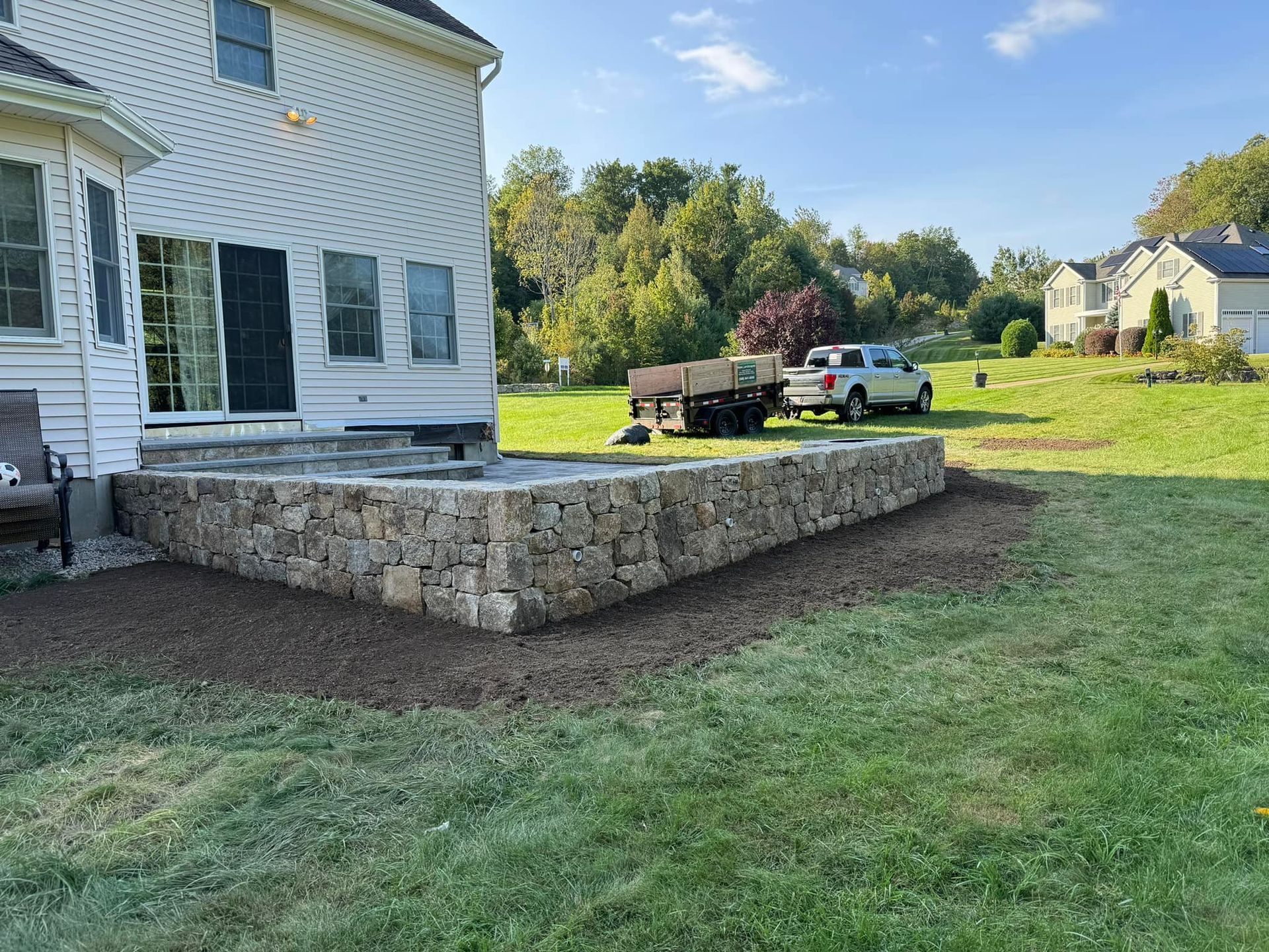 A stone wall is being built in the backyard of a house.