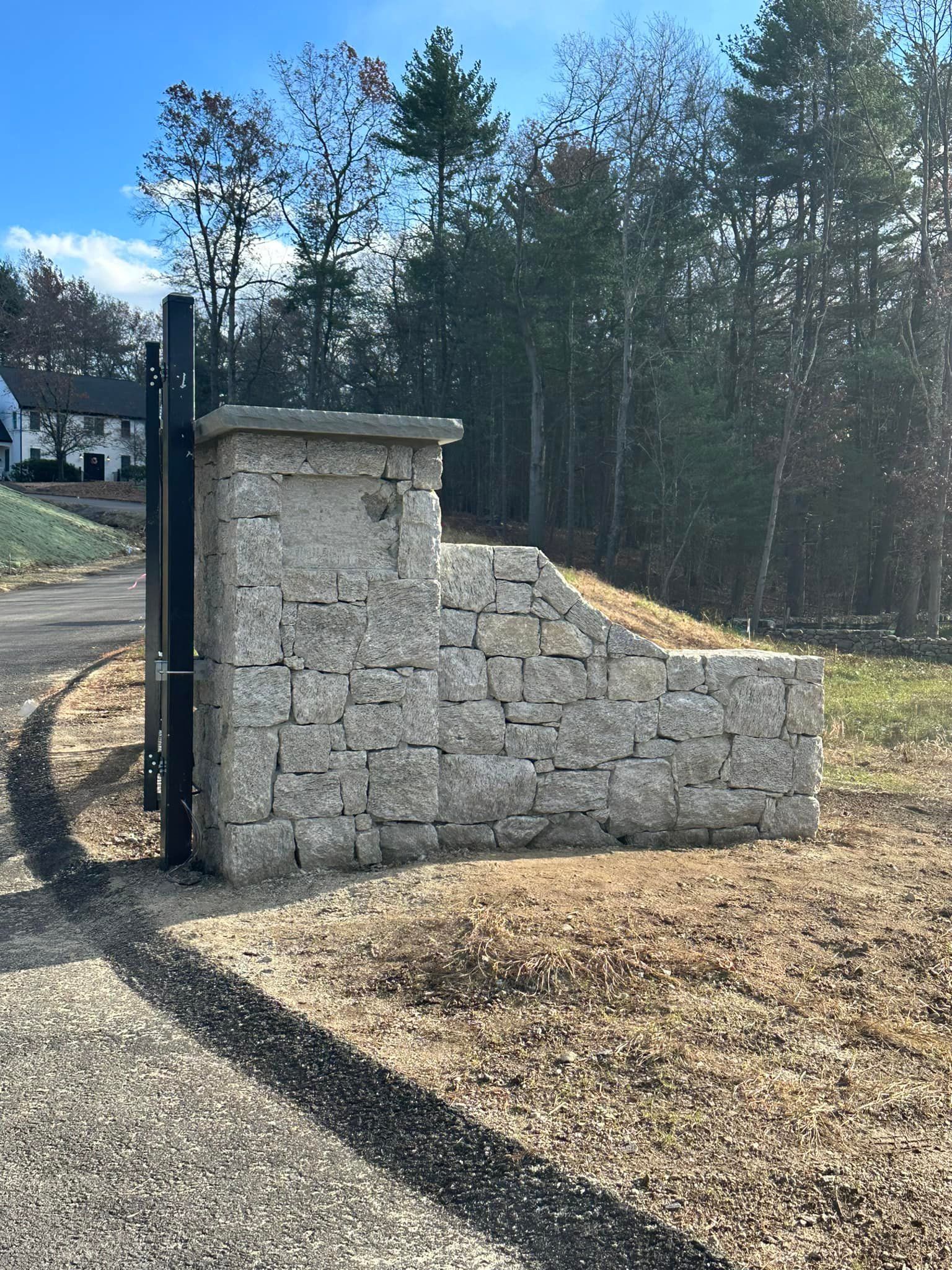 A stone wall is sitting in the middle of a dirt field next to a gate.