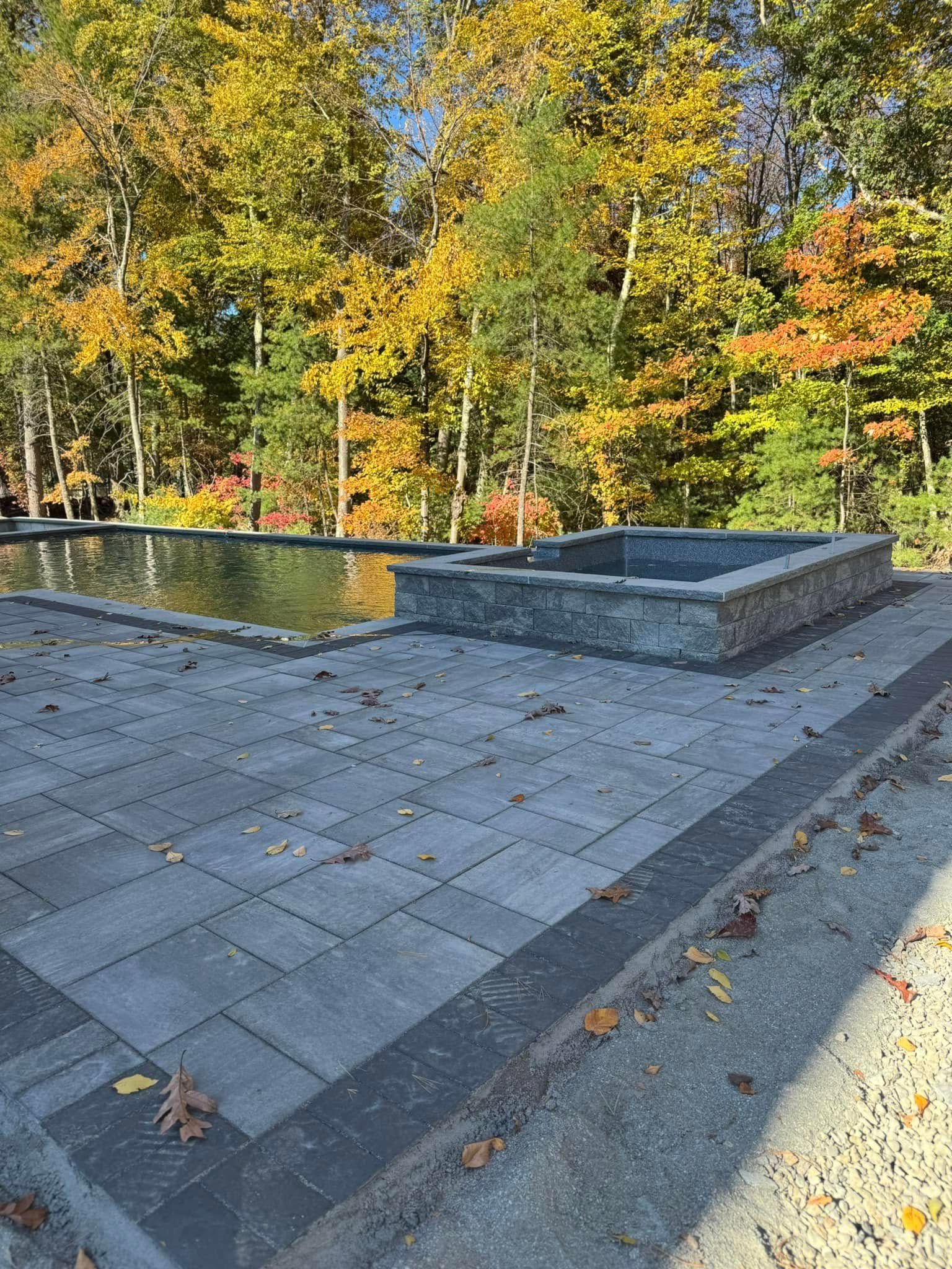A patio with a pool and trees in the background.