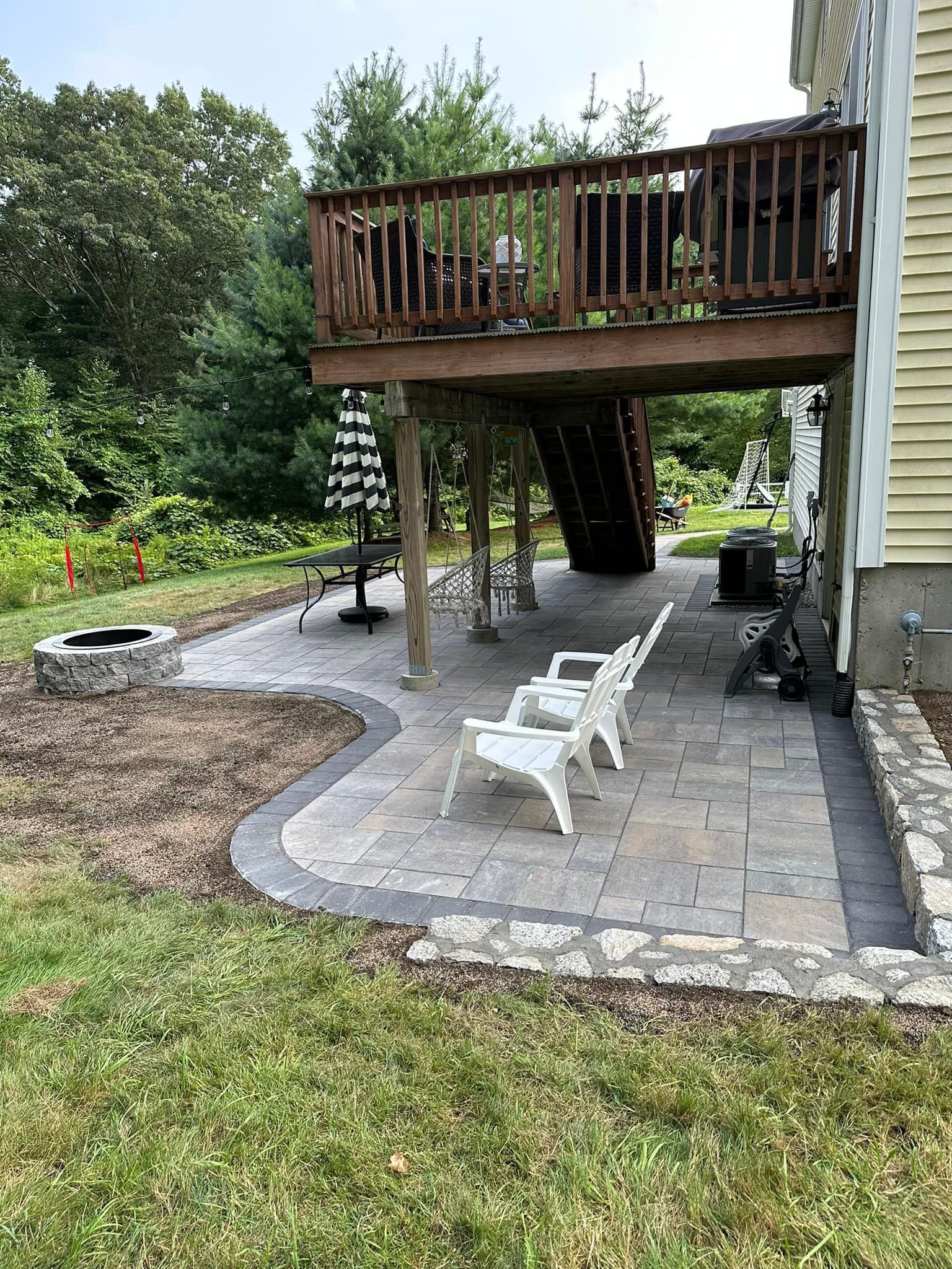 A backyard with a deck , chairs , umbrellas and a fire pit.
