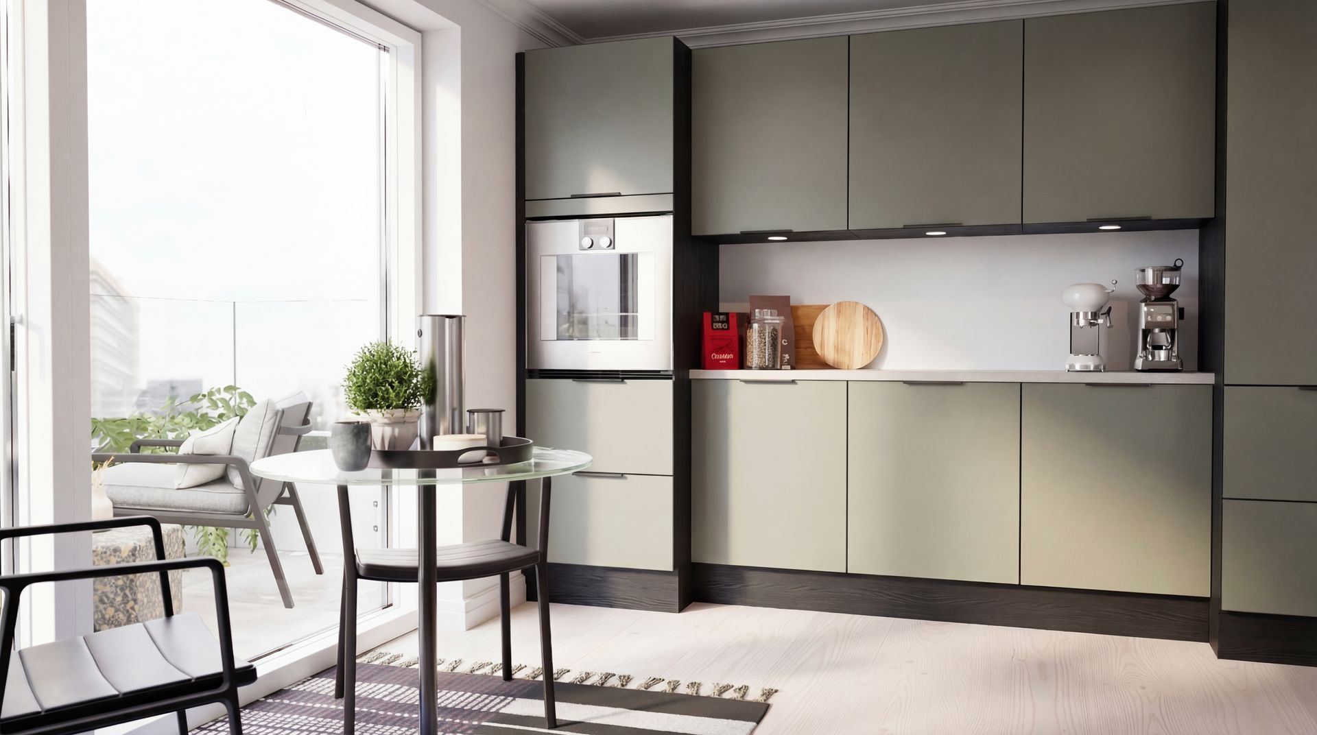 Et moderne køkken med matte salviegrønne skabe, apparater i rustfrit stål og et lille rundt bord ved en balkon.