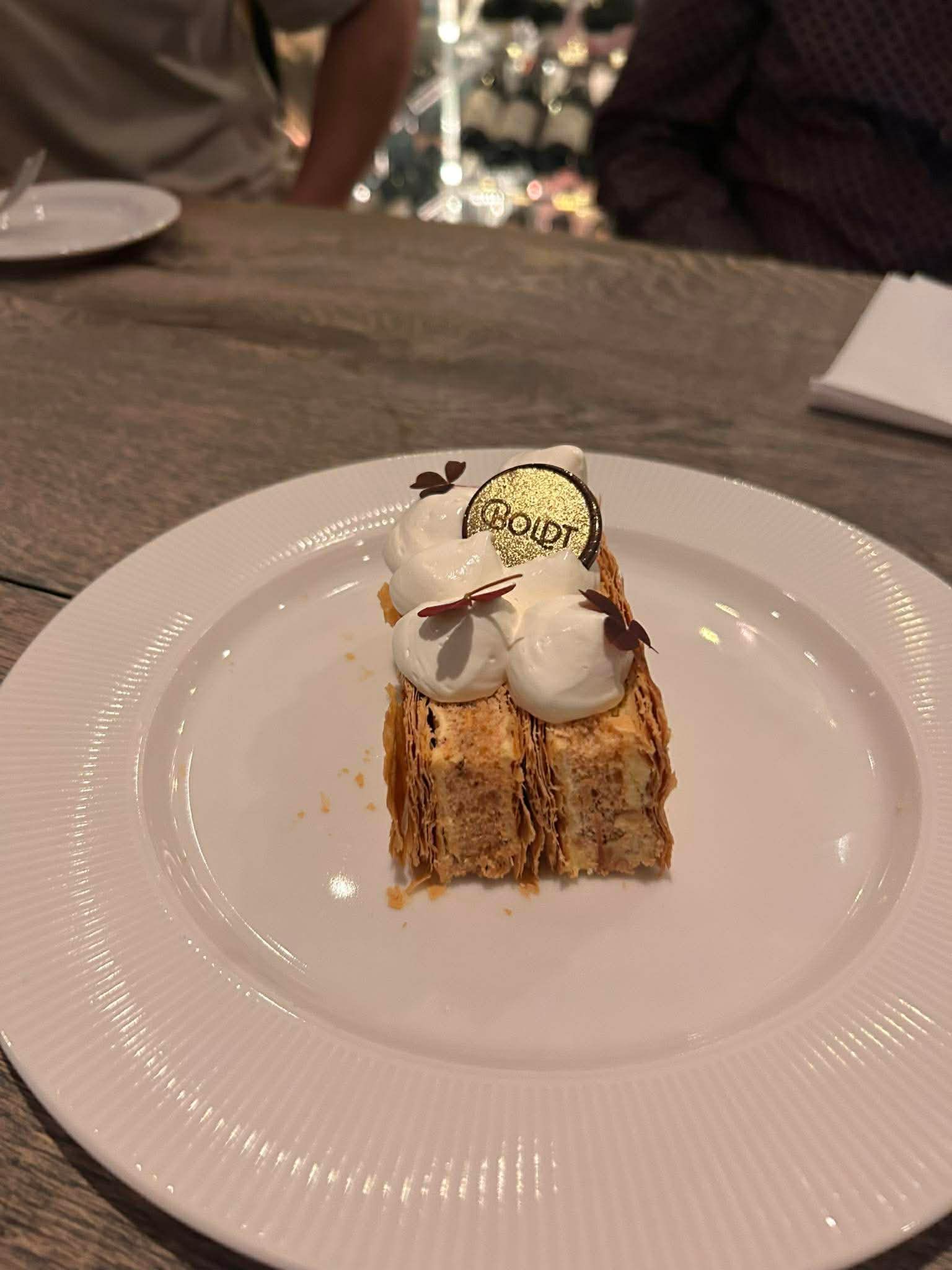 Et rektangulært stykke mille-feuille-dej toppet med flødeskum, serveret på en hvid tallerken i en spisestue.