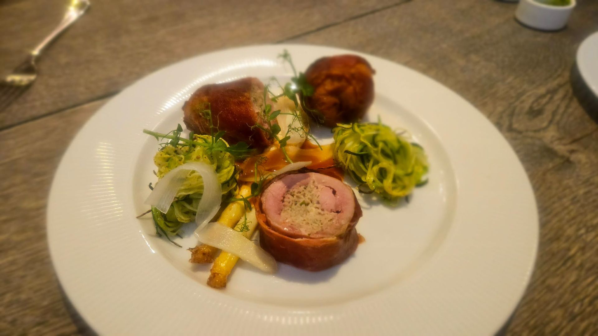 En tallerken med skiveskårne, baconindpakkede kødmedaljoner, revne grønne grøntsager og tyndt ristede gulerødder på et træbord.