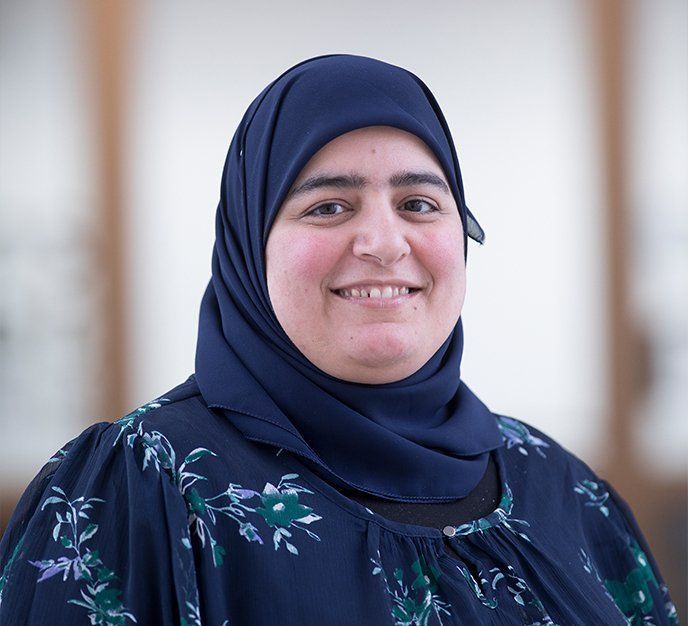 En kvinde iført blå hijab smiler til kameraet.