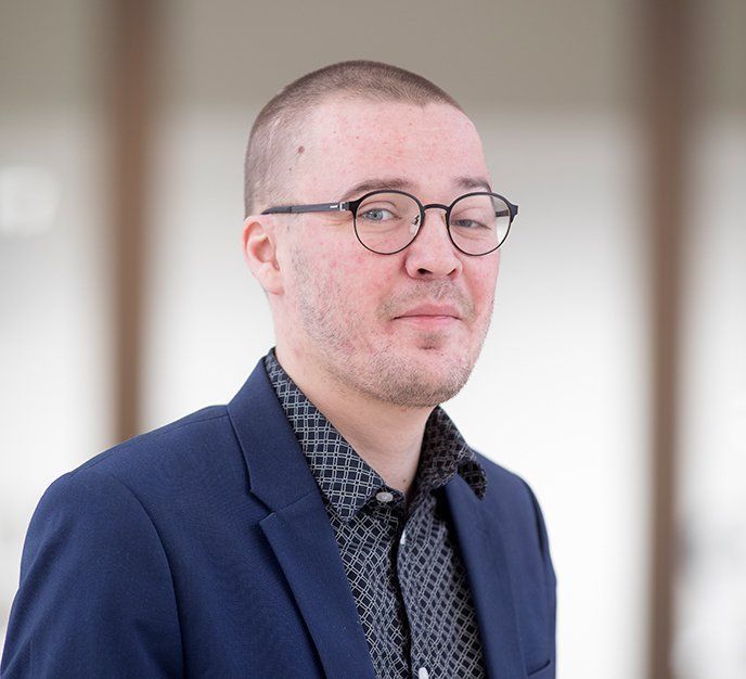 En mand iført briller og en blå jakke ser på kameraet