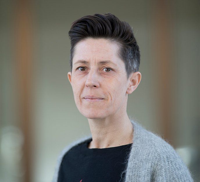 En kvinde med kort hår er iført en grå sweater og en sort skjorte.