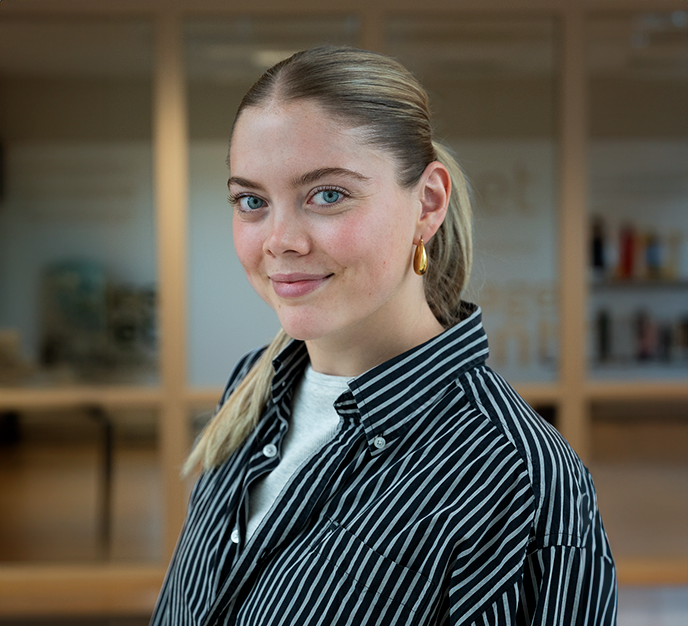 En kvinde iført en stribet skjorte og øreringe smiler til kameraet.