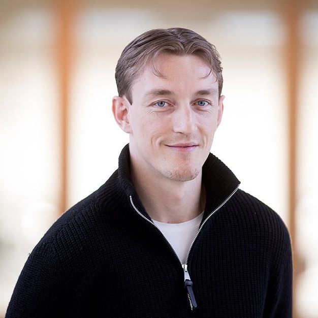 En mand iført en sort sweater smiler til kameraet