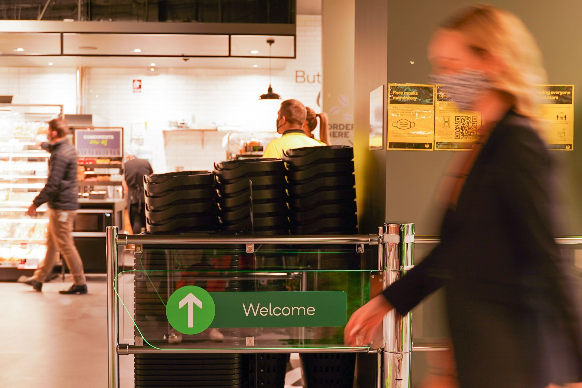 A woman wearing a mask is walking past a welcome sign in a restaurant.