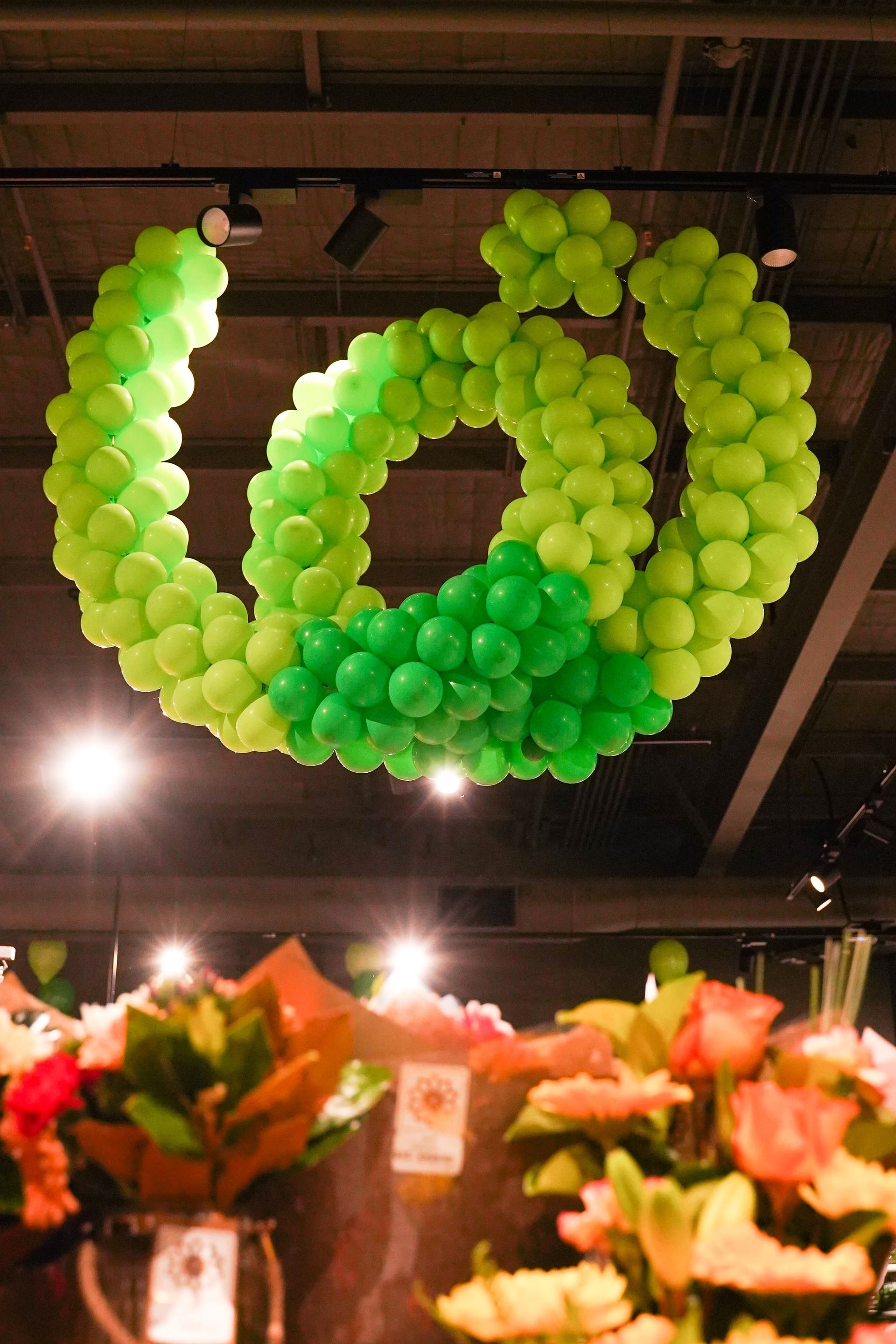 A bunch of green balloons are hanging from the ceiling
