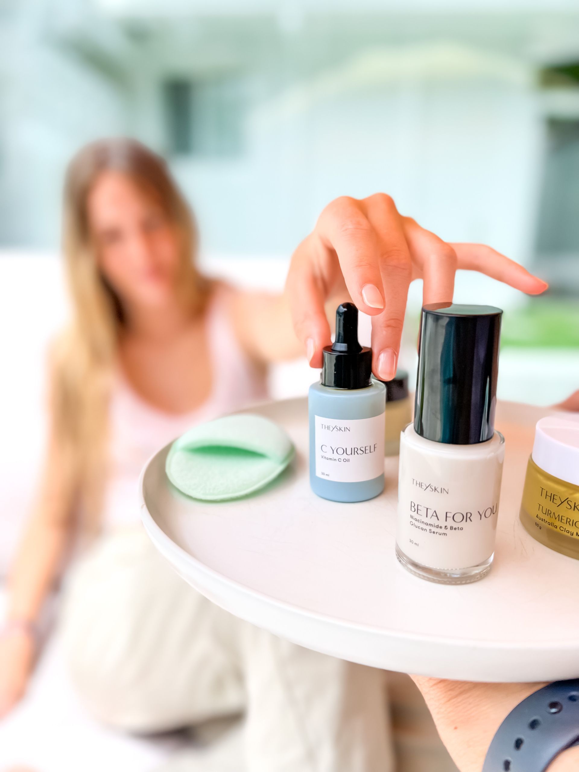 A woman is sitting on a couch while a person holds a bottle of lotion