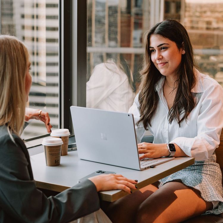 Two women are sitting at a table with a laptop.