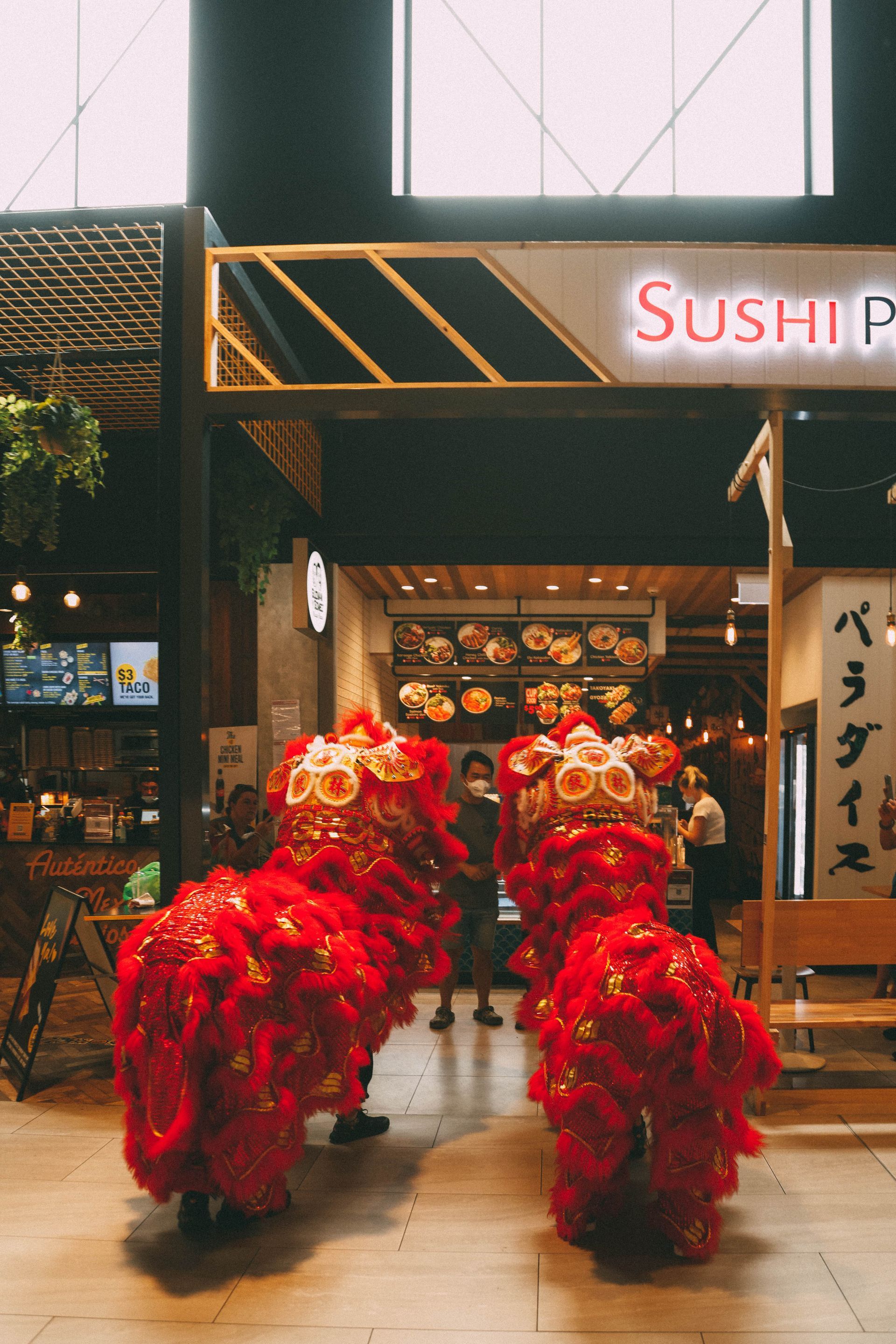 A group of people in red costumes are dancing in front of a sushi restaurant