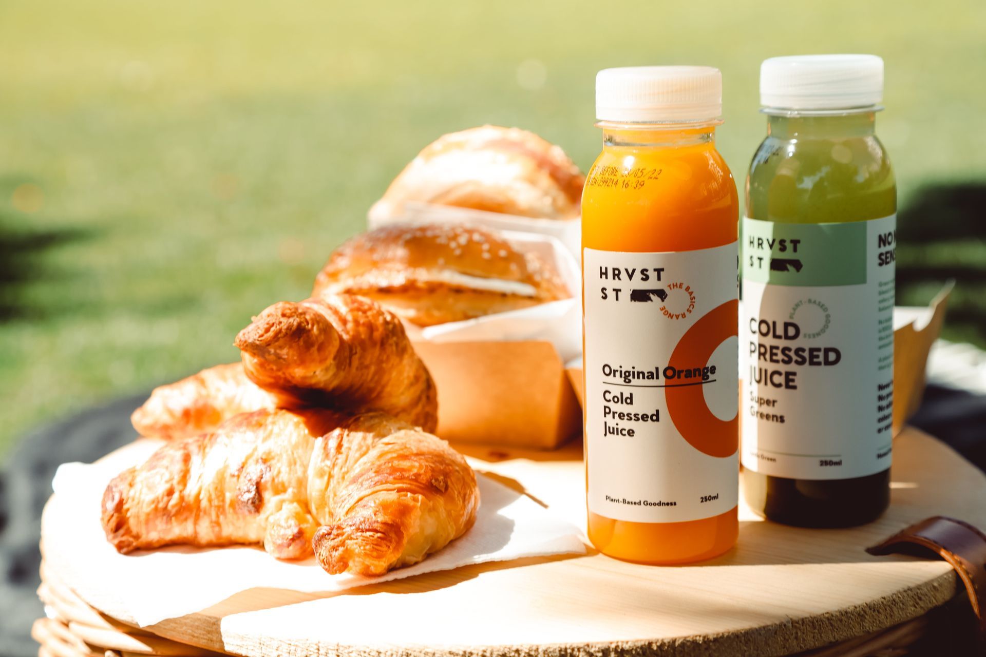Two bottles of cold pressed juice are sitting on a table next to croissants.
