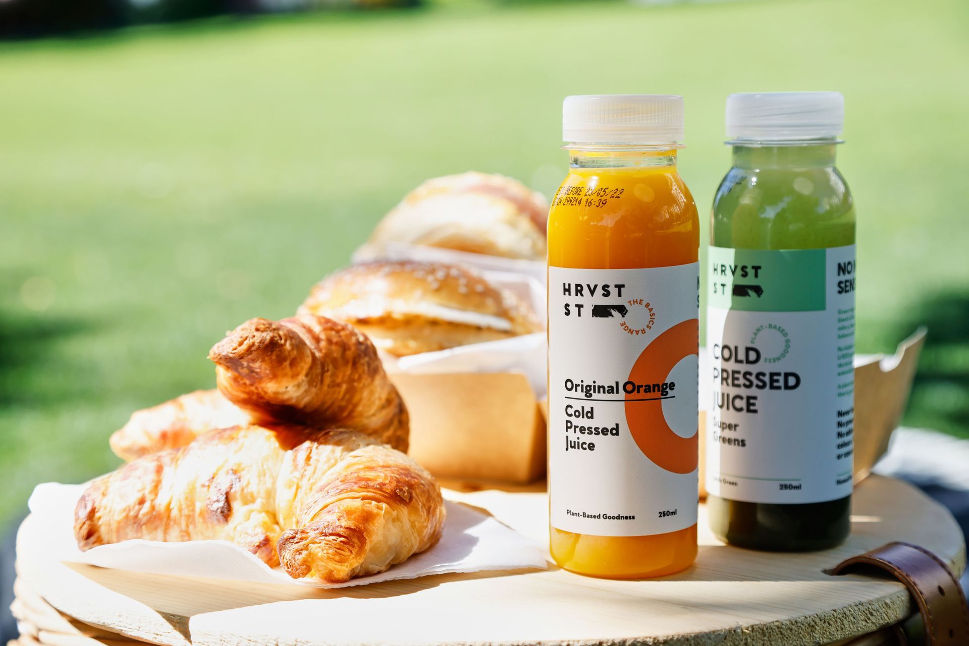 Two bottles of juice are sitting on a wooden table next to croissants.