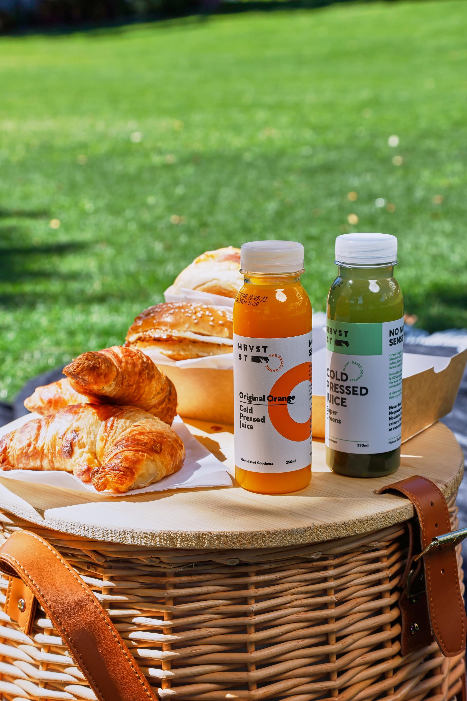 There are two bottles of juice and croissants in a picnic basket.