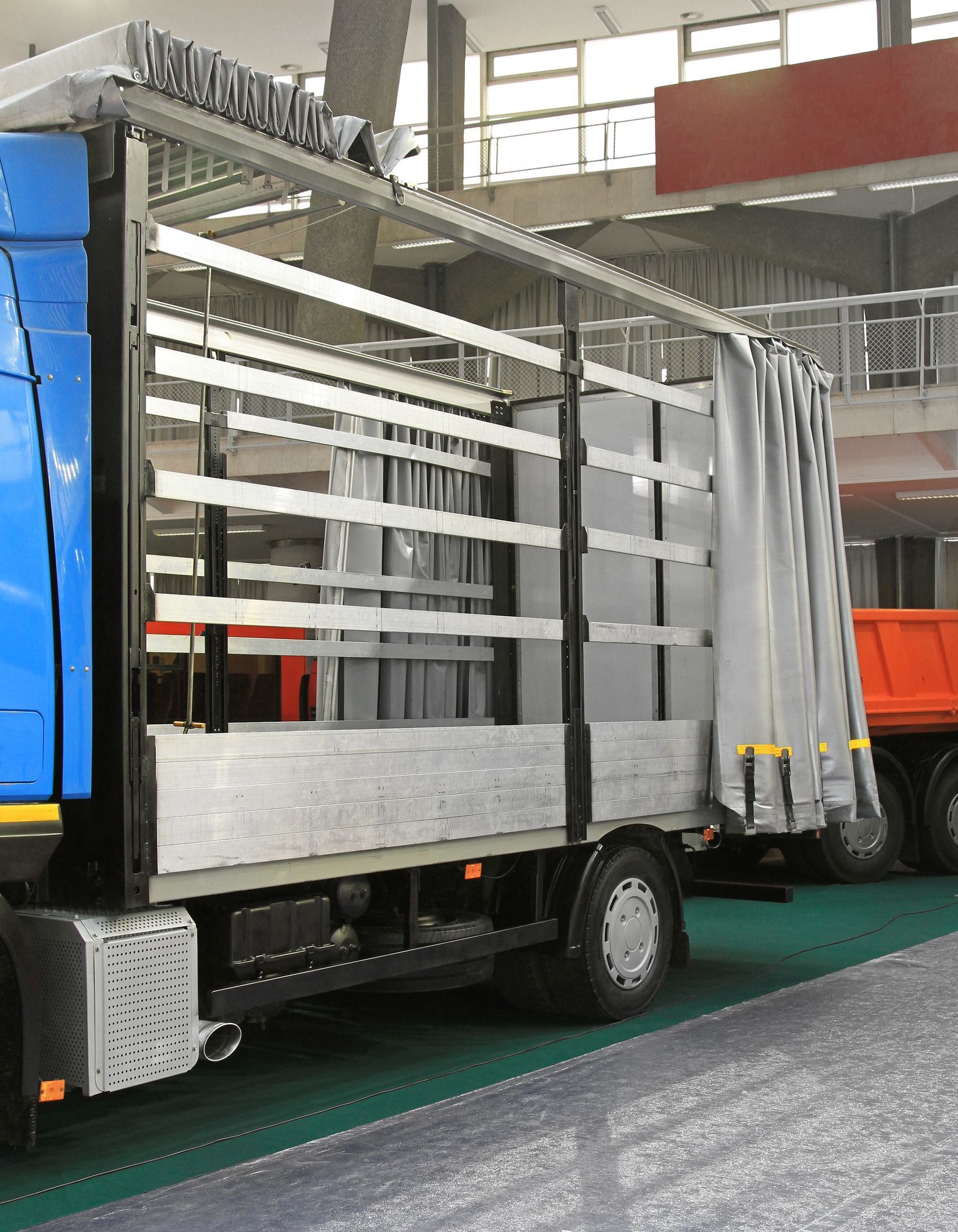 Blue truck with gray side panels and a curtain, parked inside a building.