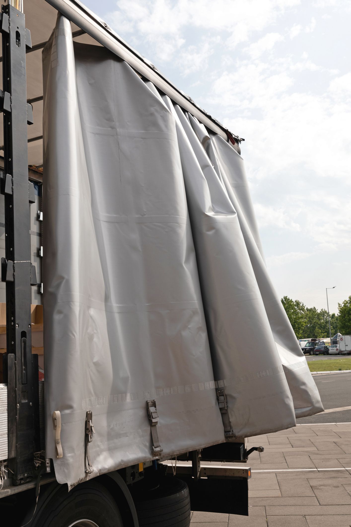 Gray truck side curtain, partially open, revealing the interior of a truck cargo area.