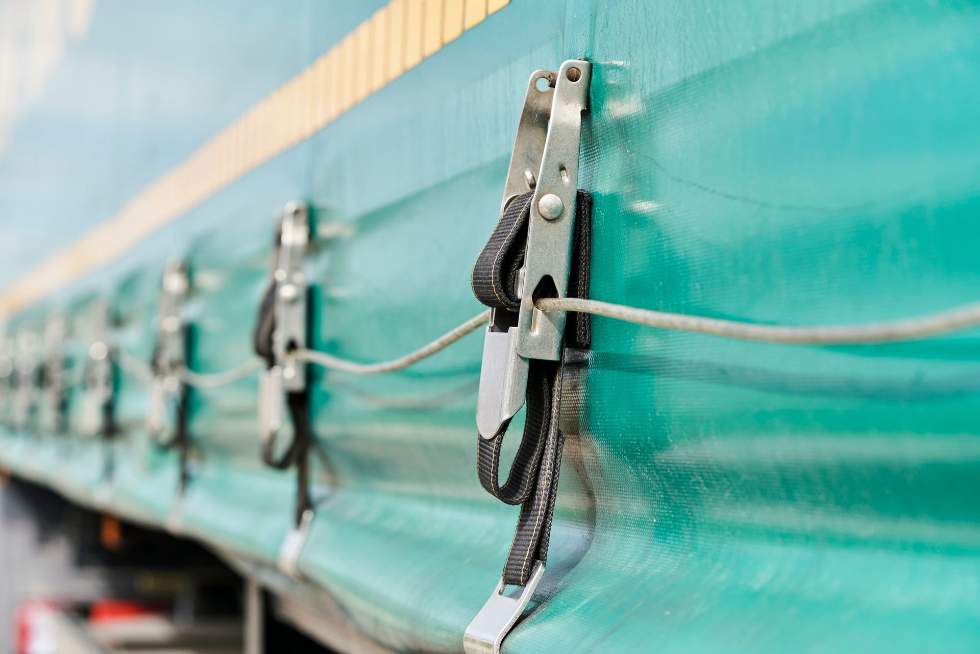 Green tarp of a semi-truck with metal clamps and cords, secured along the side.