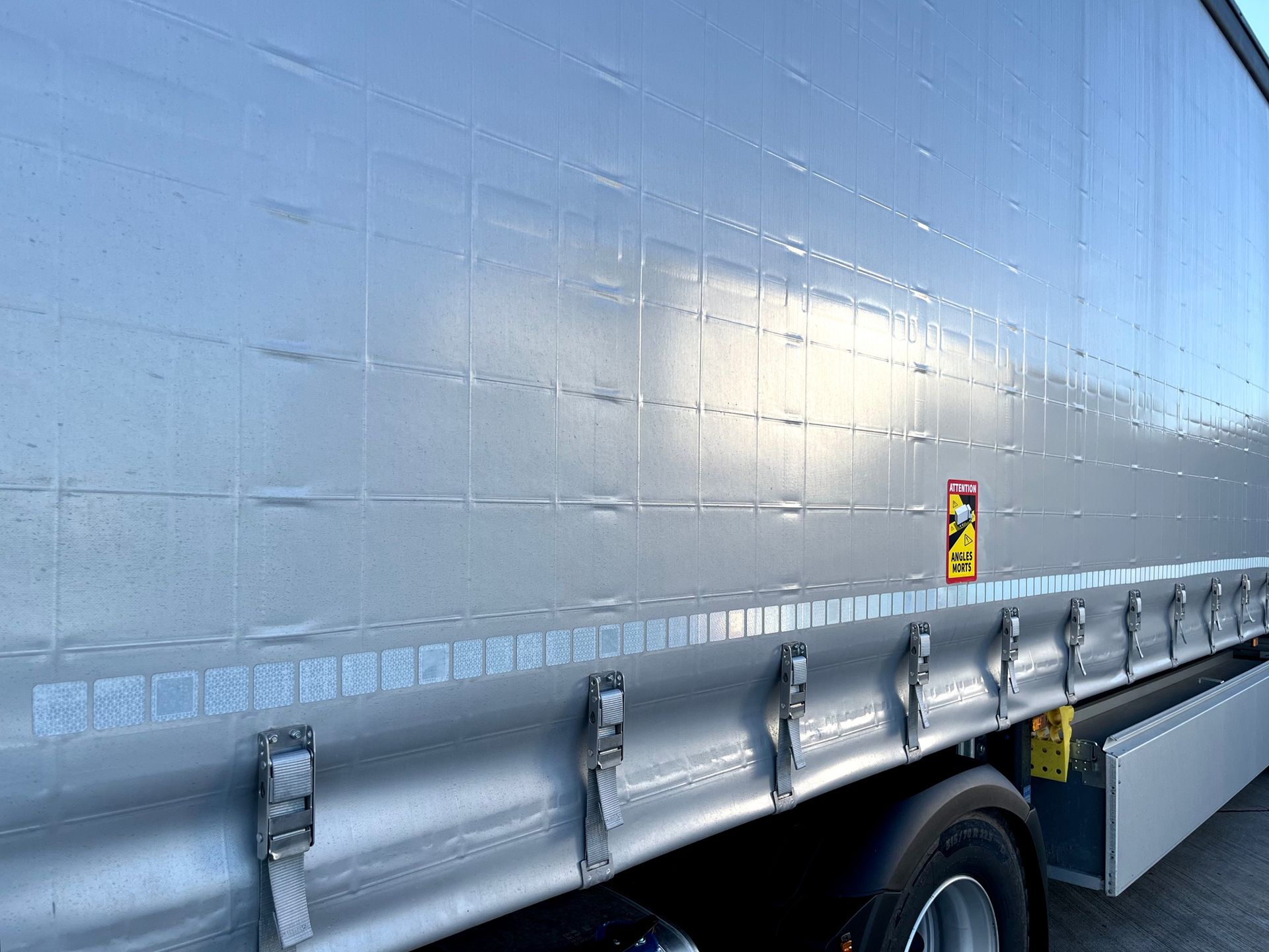 Silver truck trailer side, with buckles and warning sign.
