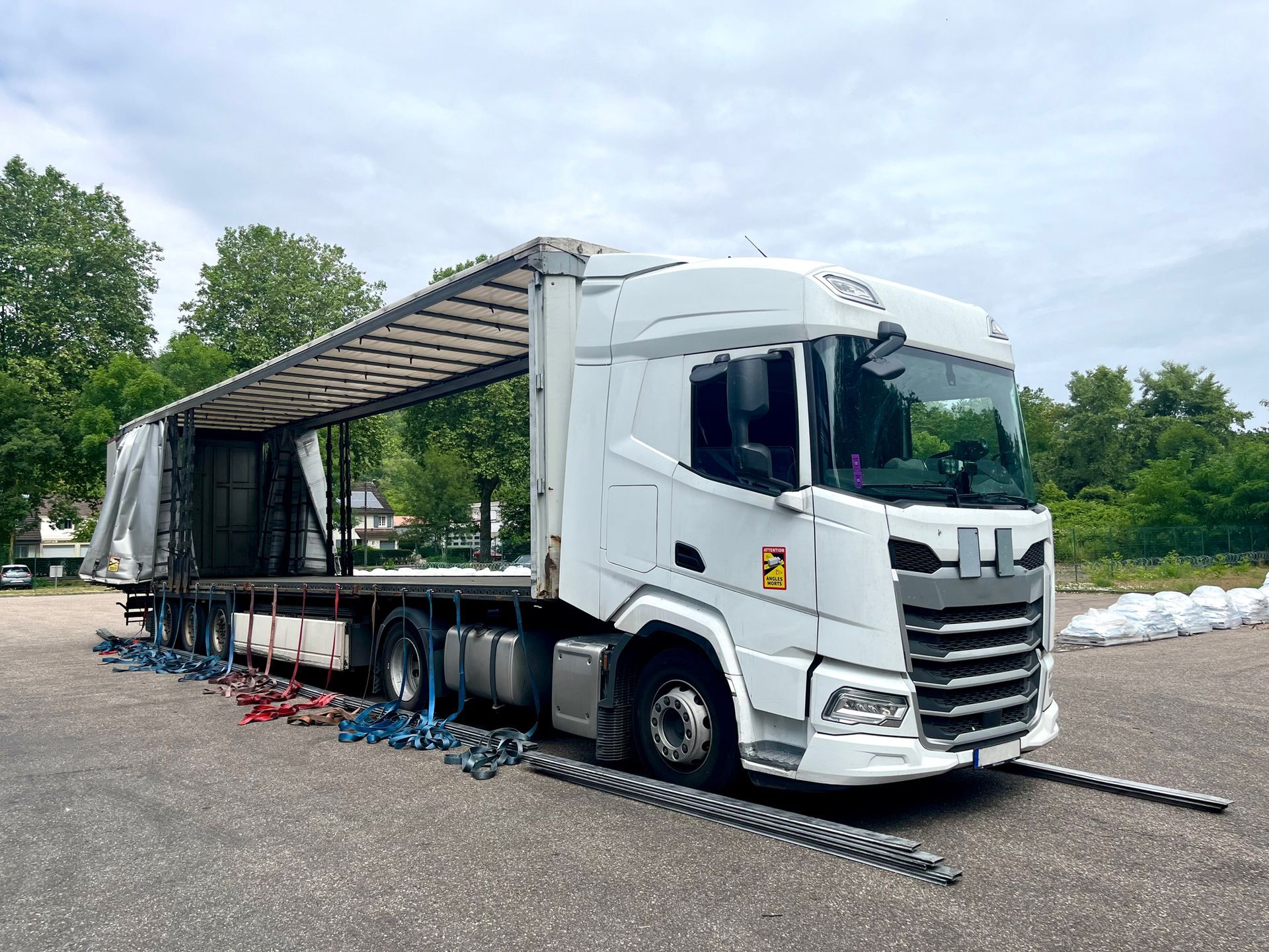 White semi-truck with an open trailer on a paved lot. The truck is parked under a cloudy sky.